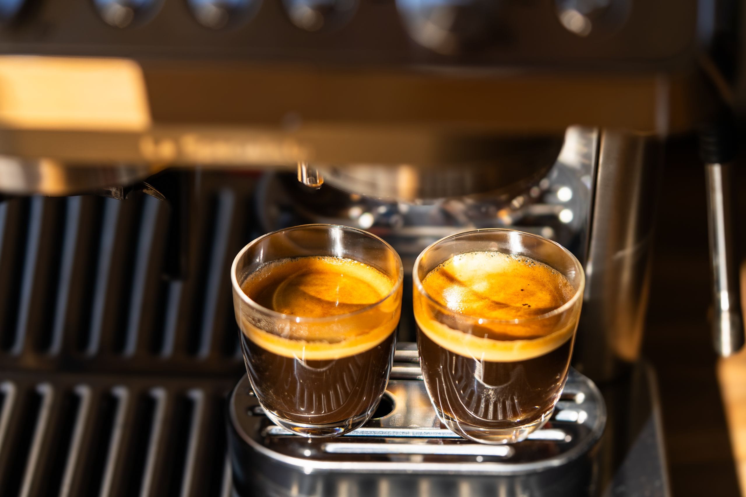 Two freshly brewed espresso shots under a modern coffee machine, highlighting crema and rich aroma.